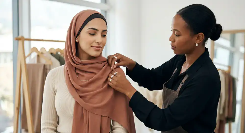 Stylist adjusting the drape of a soft earthy toned hijab